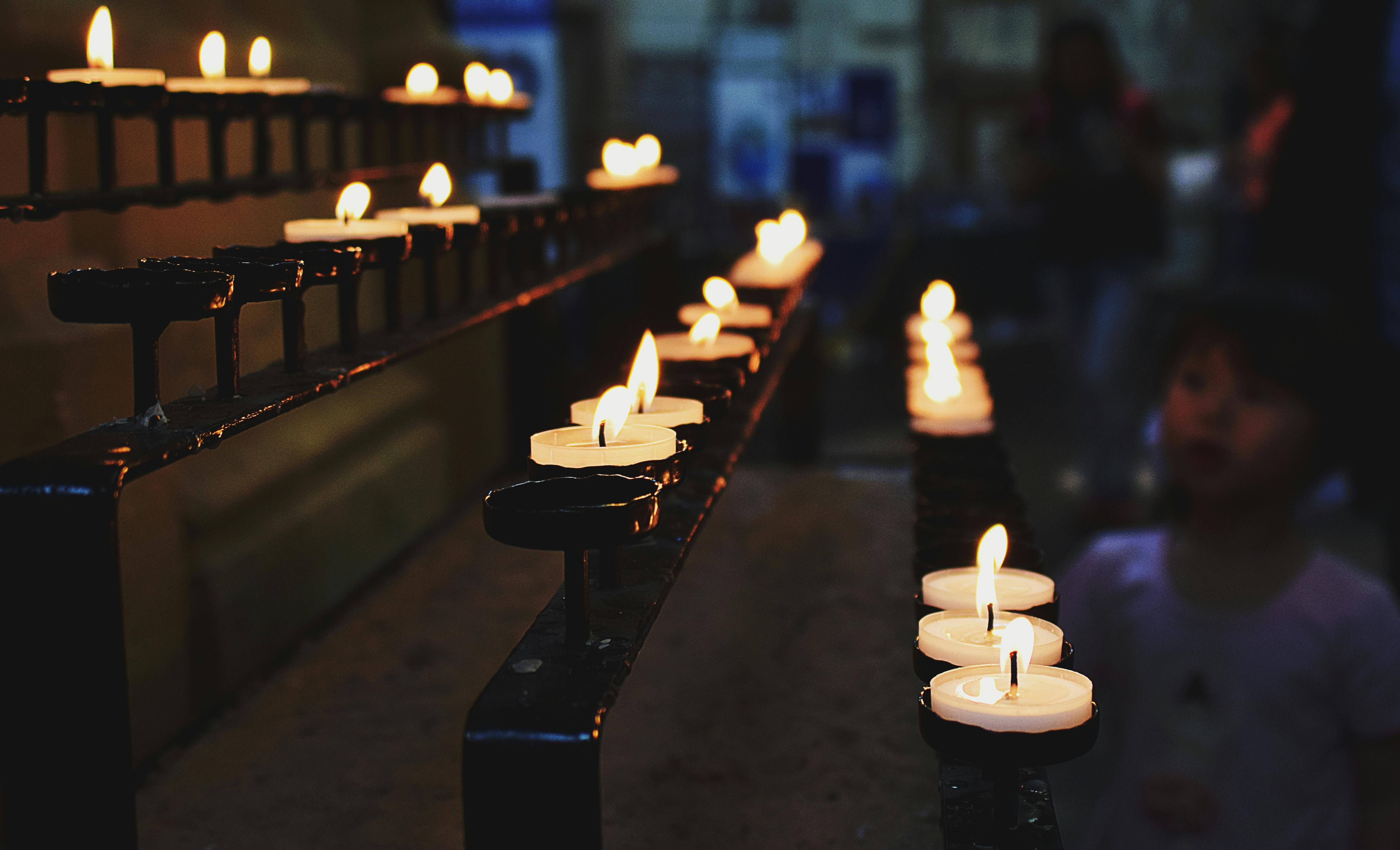 A row of lit candles in a church, with a child in the background observing.
